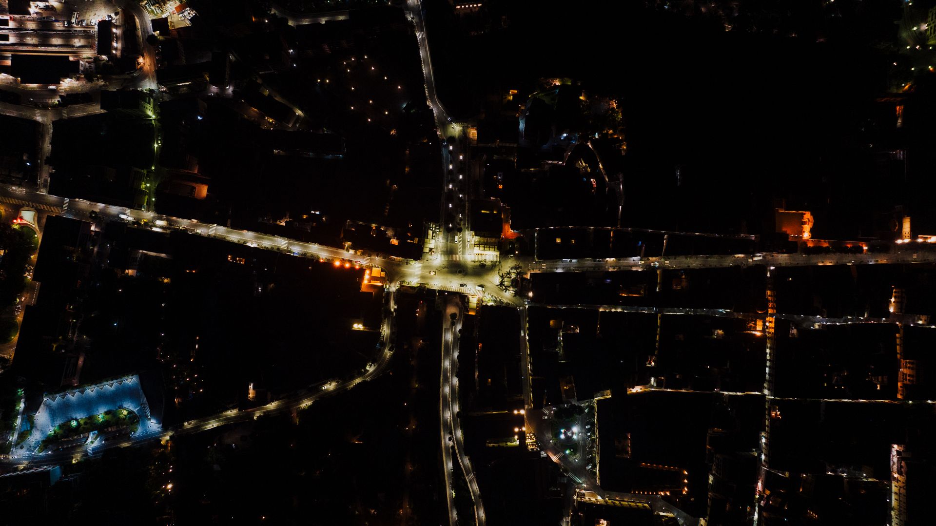 Aerial view of city streets at night, lit intersections against dark blocks